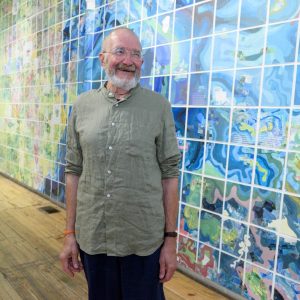 Photograph of Jerry Gretzinger smiling in front of the installation of his map panels at Intuit