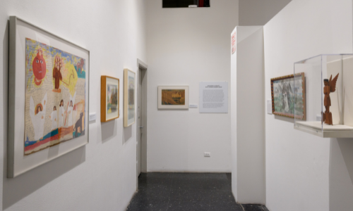 Photograph of works by Sister Gertrude Morgan, Minnie Evans and Joseph Yoakum on display with exhibition signage to the right