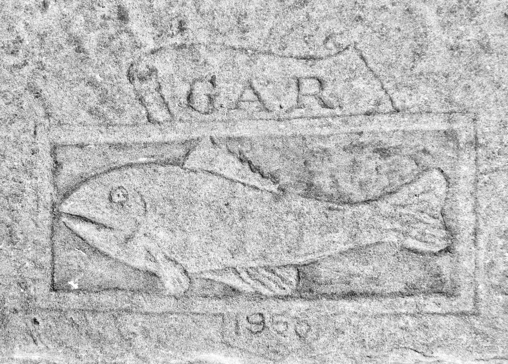 Photograph of a fish carving in light grey stone with the letters GAR engraved above