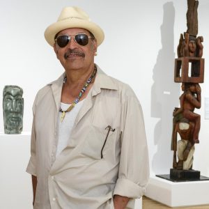 Photo of artist Roman Villarreal, standing in front of two of his sculptures in the front gallery of Intuit