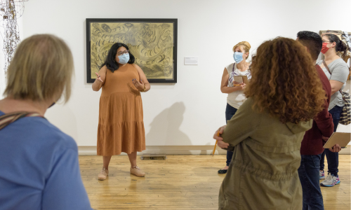 Intuit educator Paula Santos stands in front of works by Emery Blagdon and Thornton Dial in the exhibition "Trauma and Loss, Reflection and Hope"