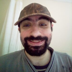 Photo of a man, identified as Motesem Mansur, smiling and wearing a baseball hat and gray shirt