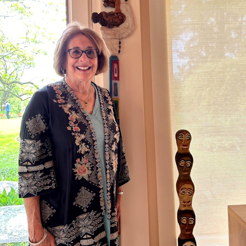 Photo of a white woman, identified as Barb Weisskopf, smiling in her home next to works of art